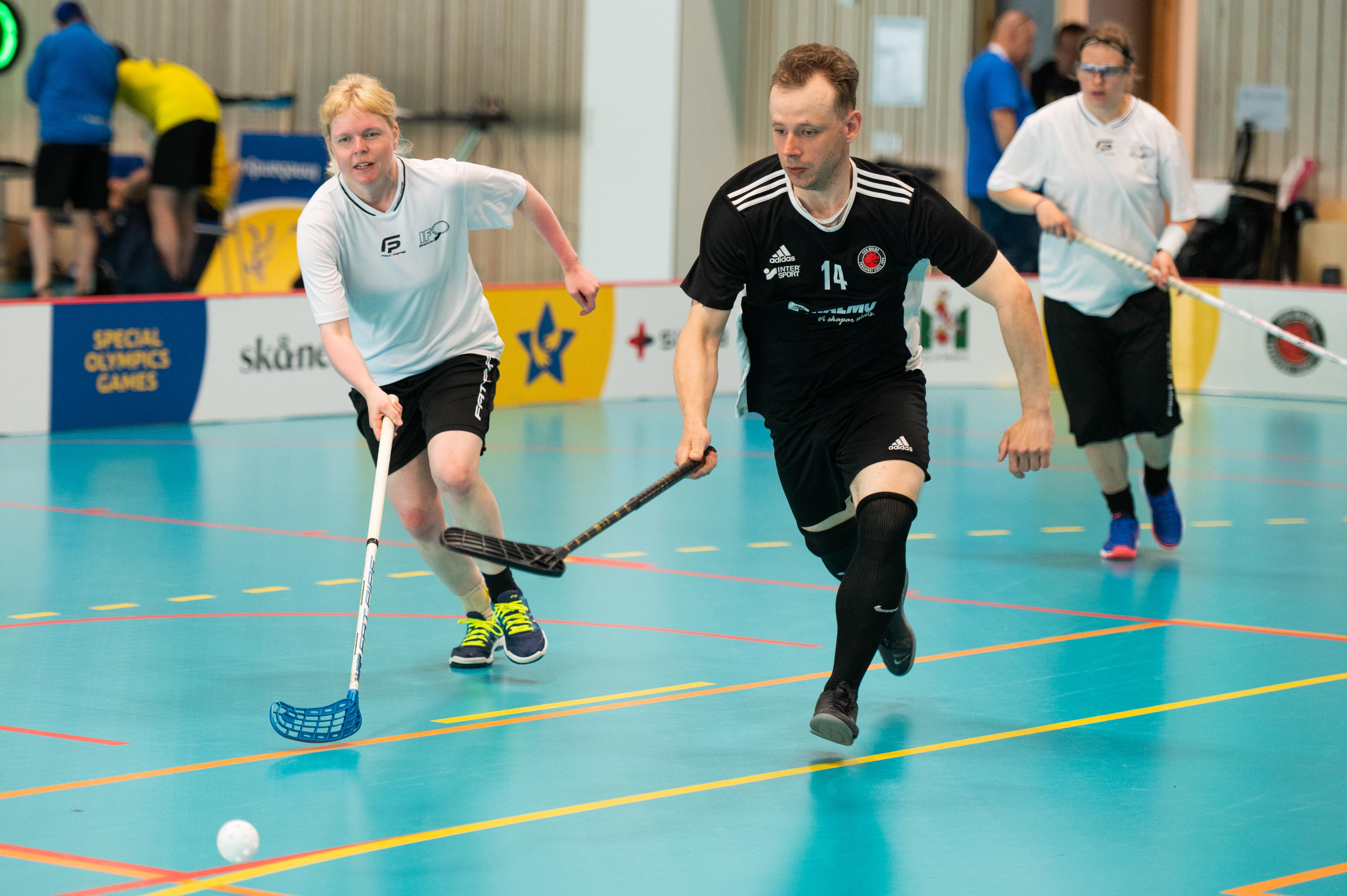 Foto, idrottshall. Innebandyspelare springer efter bollen.