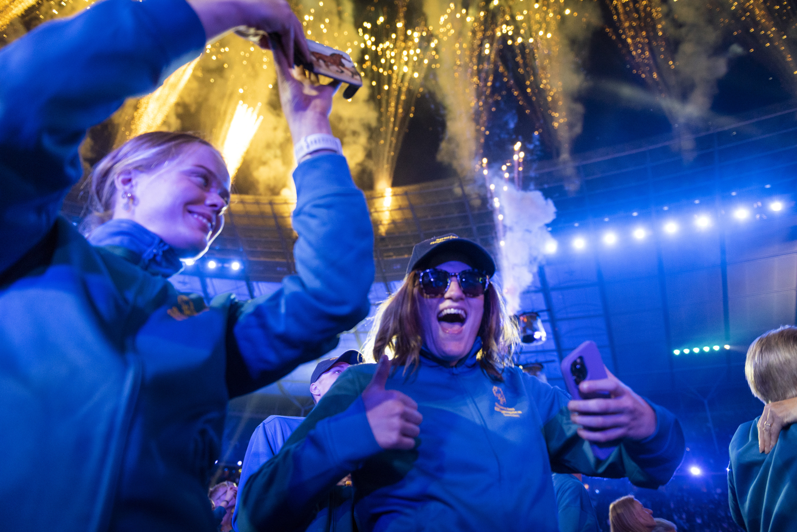Flera deltagare ler och jublar. På himlen syns fyrverkerier.