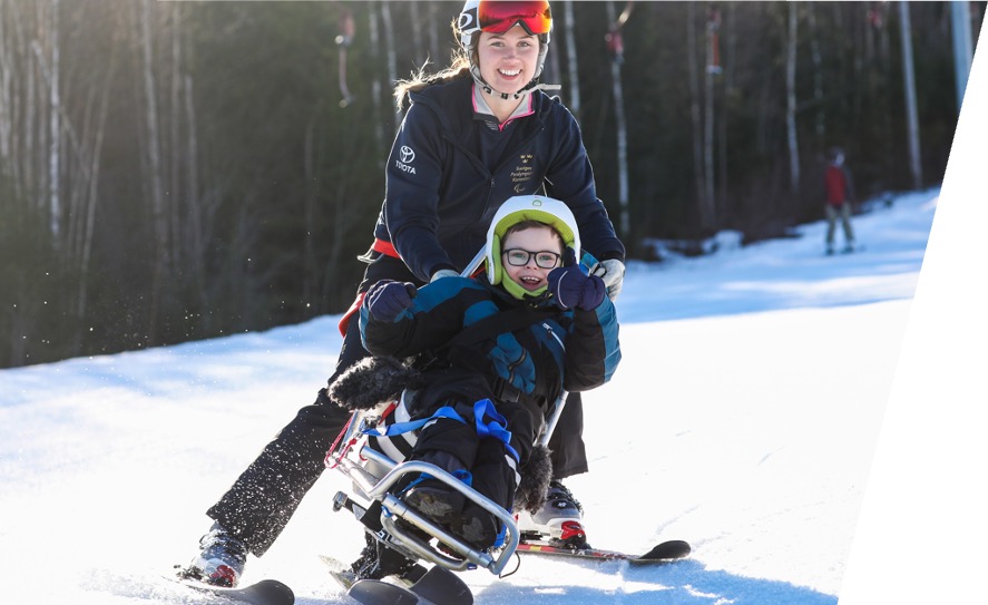 En person står på skidor och håller i en sitski med en åkare i